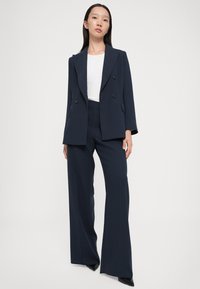 Navy double-breasted blazer with notched lapels and double-button closure, paired with wide-leg trousers in a matching fabric.
