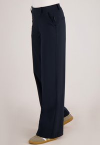 Marineblauwe, wijde broekspijpen met een gladde textuur, voorzien van zijzakken en een subtiele glans. Gemaakt van lichtgewicht, ademend materiaal.