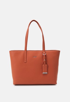 Bruine leren Calvin Klein tote tas met twee lange handgrepen en een hangend label tegen een eenvoudige lichte achtergrond.