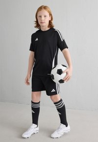 Čierny futbalový dres Adidas obsahujúci tričko s krátkym rukávom a šortky, doplnený bielymi pruhmi. Hráč drží čierno-biely futbal.