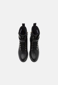 Bottines en cuir noir avec quincaillerie dorée, fermeture à lacets à l'avant et fermeture éclair à l'arrière. Détails texturés au niveau de la cheville et finition lisse.