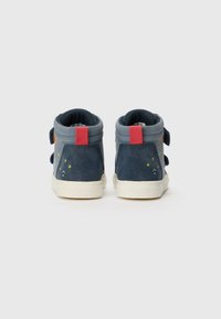 Mörkblå mocka högtoppsneakers med röda häldetaljer och kardborreband. Har stjärnmönster i gult och orange på sidorna.