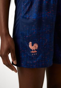 Navy blue shorts with a textured pattern of red and blue speckles. Features a cream-colored rooster emblem with "FFF" on a shield.