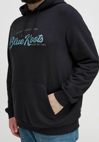 Schwarzer Hoodie mit einer Vorderentasche, versehen mit einem türkisfarbenen "Blue Roots"-Logo. Weicher Stoff, Kapuze mit Kordelzug und gerippte Bündchen.