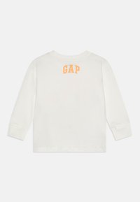 White long-sleeve shirt featuring the word "GAP" in arching orange text on the upper back. Made from soft cotton material.