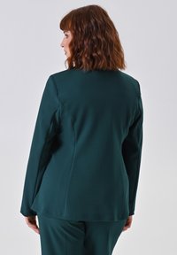 Donkergroene blazer met een soepele, op maat gemaakte pasvorm, lange mouwen en een lichte flair aan de onderkant, ontworpen voor een strakke, professionele uitstraling.