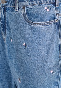 Mėlyni džinsiniai šortai, turintys laisvą siluetą, papuošti siuvinėtosiomis rožinėmis vyšniomis ir kontrastingomis siūlėmis. Matomas priekinis kišenė.