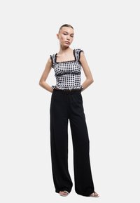 Geruite zwart-witte top met ruches aan de mouwen en zwarte accenten, gecombineerd met hoge taille zwarte wijde broek en lichte sandalen.