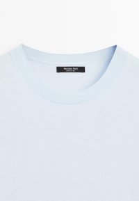 Maglione azzurro chiaro con scollatura rotonda, con un'etichetta nera che recita "Massimo Dutti" cucita al colletto.