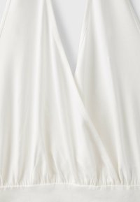 Haut blanc à col en V style portefeuille avec ourlet élastique froncé et texture de tissu douce et lisse.