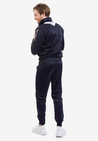 Tuta da ginnastica blu navy realizzata in un tessuto morbido, con colletto alto, dettagli bianchi e pantaloni affusolati con orli a costina. Sneakers bianche.