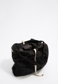 Czarna torba na ramię z tkaniny z siateczkowym dolnym panelem, wyposażona w beżowy pasek i zatrzask. Wnętrze jest miękkie, niepodszewkowe i przestronne.