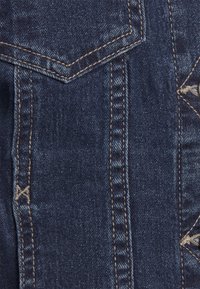Denimtyg i mörkblått med framträdande sömmar och en texturerad yta. Har mönsterdetaljer nära den högra kanten.