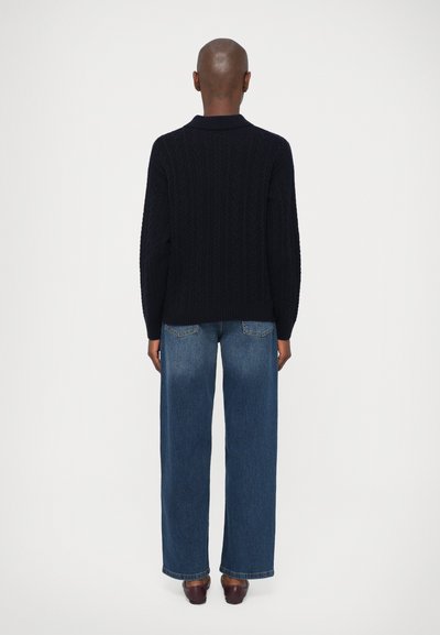 Marineblå kabelstrikket genser med krage, kombinert med høyere midje, vid bukse i blå denim, båret med brune sko.