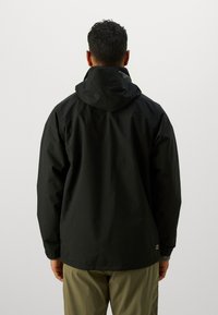 Jachetă tip windbreaker în negru, fabricată dintr-un material ușor. Are glugă, mâneci lungi și o croială lejeră. Branding minim la tiv.
