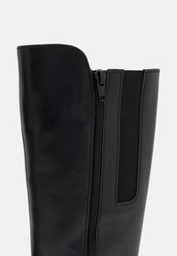 Stivale in pelle nera con altezze verticali, chiusura con cerniera e pannello elastico laterale per una vestibilità regolabile e facile da indossare.