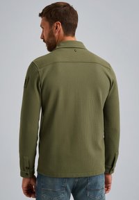 Olijfgroene gebreide jas met een gestructureerde afwerking, een kraag en knoopmanchetten. Uitgerust met een logo op de achterkant en een getailleerde pasvorm.