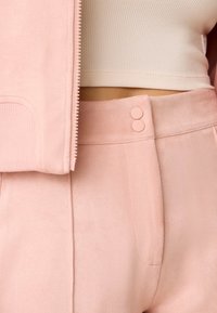 Giacca in tessuto rosa chiaro e morbido e pantaloni abbinati a vita alta con una texture liscia, tasche frontali e due bottoni decorativi.