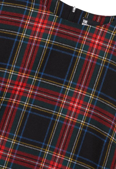 Primo piano di un tessuto nero con un motivo a scacchi tartan in rosso, blu, verde, giallo e bianco, e una cerniera visibile in cima.