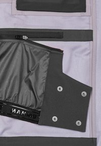 Flerfärgade tygskikt i lila och grått med dragkedjor och knappar; glänsande svart inre foder synligt. Texturerade ytor och minimalistisk design.