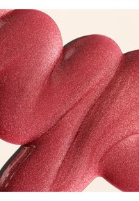 Échantillon de rouge à lèvres liquide rose-rouge scintillant avec une texture lisse et brillante sur fond beige.