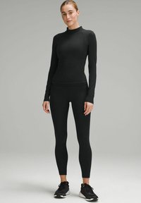 Czarny top z długim rękawem i półgolfem, w zestawieniu z czarnymi, dopasowanymi legginsami. Materiał wydaje się gładki i elastyczny, odpowiedni do odzieży sportowej.