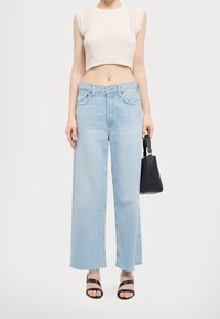 Kremowy, krótki sweter dzianinowy z krótkimi rękawami, zestawiony z jasnoniebieskimi, szerokimi spodniami dżinsowymi z postrzępionymi brzegami oraz czarną torebką. Czarne sandały na paski.