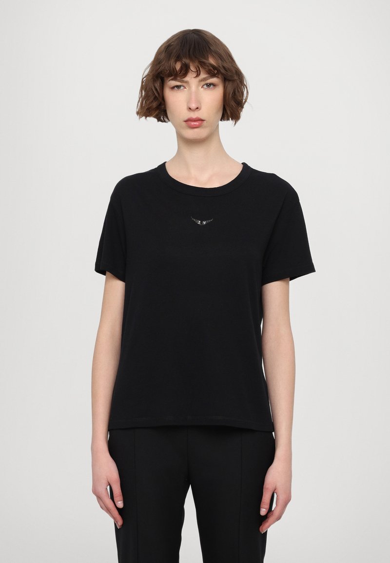 T-shirt en coton noir avec un col rond, des manches courtes et un subtil emblème d'aigle brodé sur la poitrine. Texture lisse et coupe décontractée.