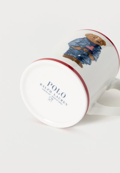 Cana din porțelan alb cu un ursuleț de pluș îmbrăcat într-un costum albastru, ținând un drapel american; cu marca "Polo Ralph Lauren" pe partea inferioară.