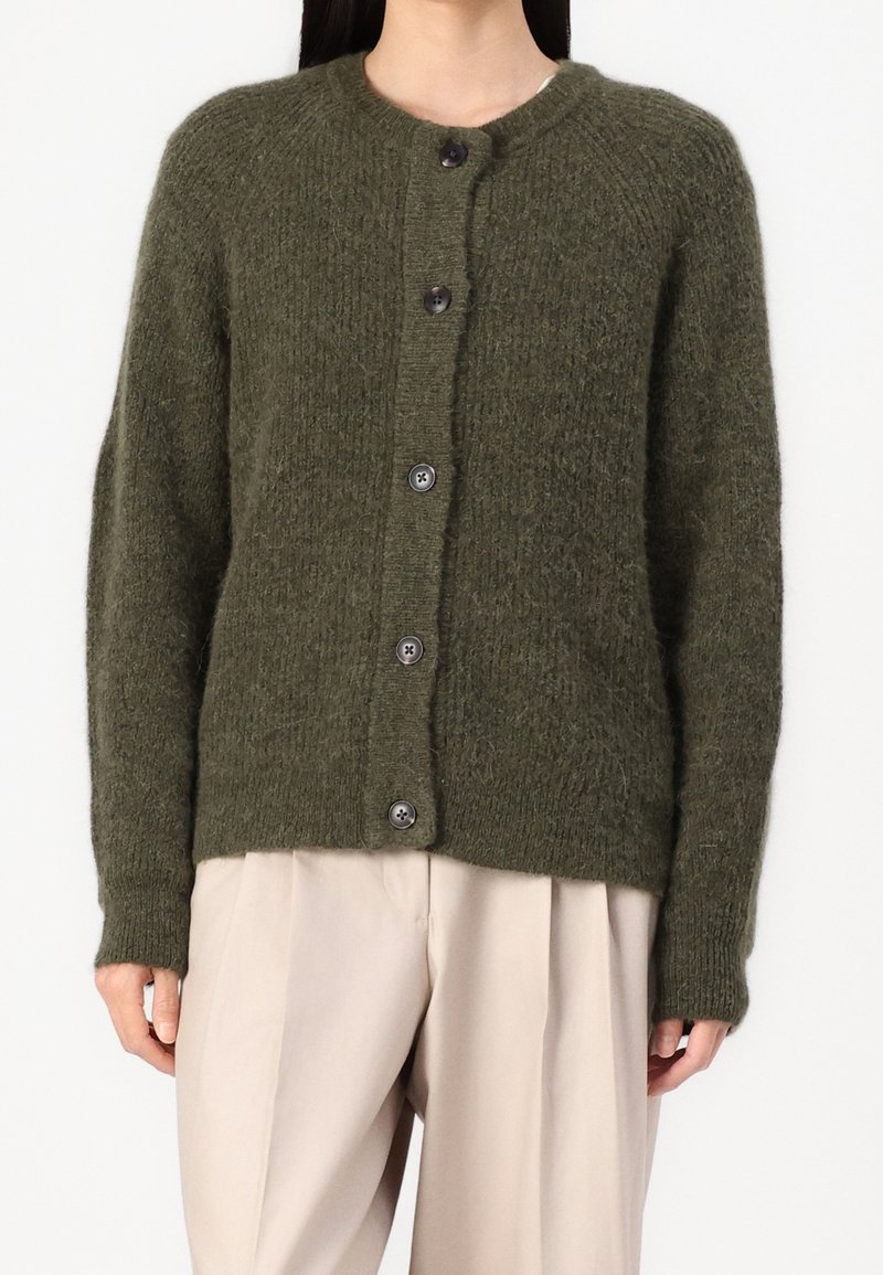 Olivewoska zielona kardiganka wykonana z teksturowanej dzianiny, z okrągłym dekoltem, guzikami z przodu i długimi rękawami, w zestawie z beżowymi spodniami.