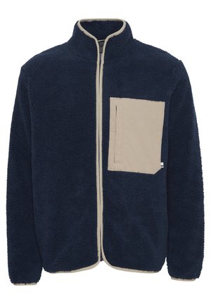 Giacca in pile blu navy con colletto alto, zip crema e tasca sul petto. Presenta un tessuto morbido e testurizzato e dettagli a contrasto nella tasca.