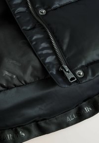 Svart puffjacka med en slät, glansig yta. Har en silverfärgad dragkedja, märkesbälte och präglad logotypdetalj.