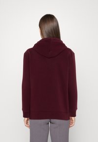 Sudadera con capucha burdeos de mangas largas, con puños y dobladillo acanalados. Material de mezcla de algodón con una textura suave, vista desde la parte de atrás.