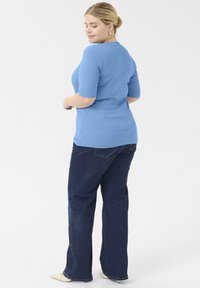 Top ajustado de canalé azul claro con mangas cortas, combinado con jeans de campana azul oscuro. Acentos mínimos y textura suave.