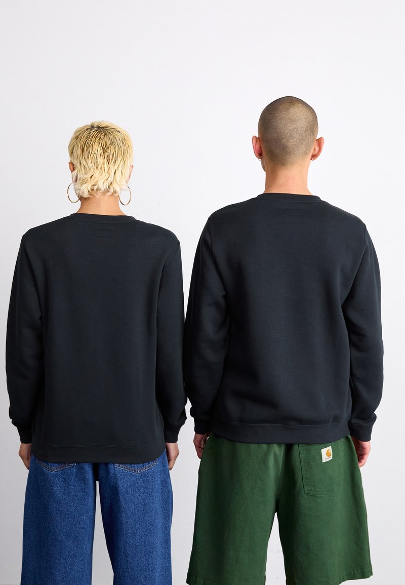 Sudaderas negras de tela suave, con puños y dobladillo acanalados, combinadas con vaqueros azules y pantalones cortos verdes, vistas desde atrás.