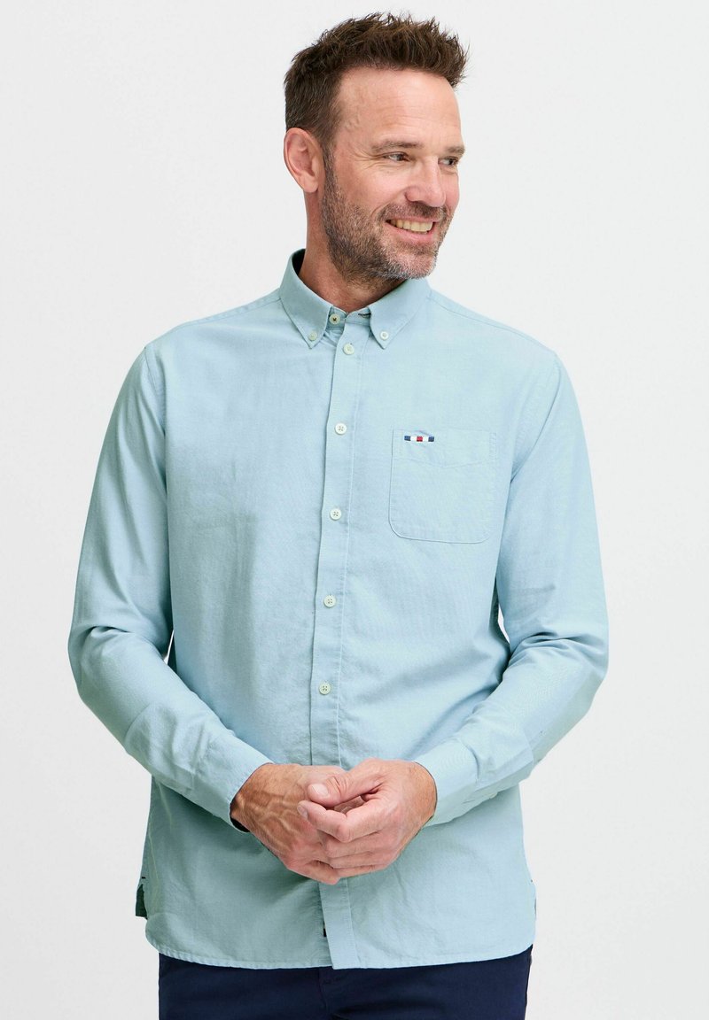 Camicia azzurra chiara in un tessuto morbido, con taschino sul petto a righe e colletto button-down, indossata da un modello.