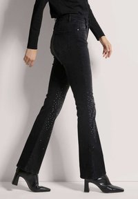 Zwarte flared jeans met strassdetails langs de zijkanten, gemaakt van denimstof. Draag met puntige zwarte enkelhakken.