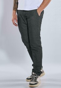 Dark grey cotton pants with a slim fit, featuring side pockets and contrasting stitching, paired with light-colored high-top sneakers.