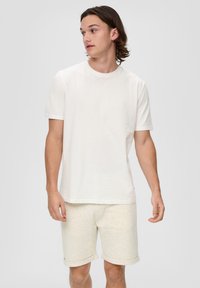 Weißes Baumwoll-T-Shirt mit kurzen Ärmeln, rundem Ausschnitt und schlichter Gestaltung, kombiniert mit hellbeigen Shorts mit umgeschlagenen Säumen und weichem Material.
