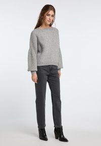 Grauer Strickpullover mit weiten, gerippten Ärmeln, kombiniert mit engen schwarzen Jeans und Stiefeletten mit Absatz. Die Textur wirkt weich und gemütlich.