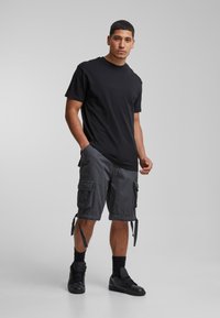 T-shirt en coton noir associé à un short cargo gris foncé avec poches latérales et cordons. Porté avec des baskets noires et des chaussettes de cheville.
