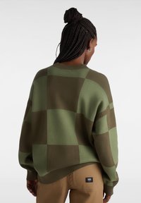 Grön och brun oversized stickad tröja med rutigt mönster, rund halsringning och texturerat garn. Synlig etikett på fållen.