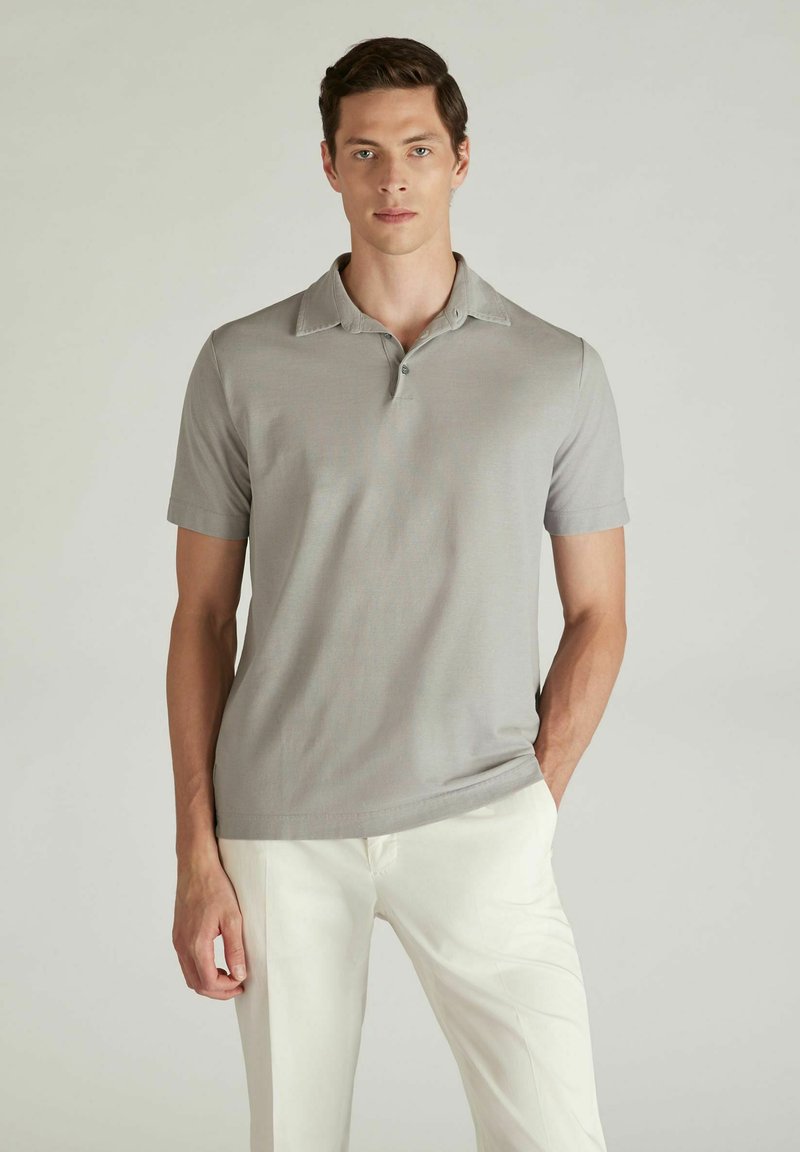 Polo shirt grigio chiaro con patta bottonata, maniche corte e una morbida texture, abbinato a pantaloni bianchi. Design semplice senza motivi.
