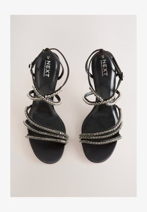 Juodos dirželiais susegamos basutės su metaliniais akcentais. Turi lygią tekstūruotą pado dalį ir kelias papuoštas dirželius, suteikiančias sluoksniuotą išvaizdą.