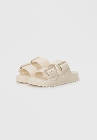 Sandali leggeri beige chiaro realizzati in gomma, con due cinturini regolabili, punta arrotondata e suola testurizzata caratterizzata da piccole scanalature per la trazione.