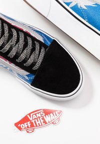 Baskets bleu et noir avec un embout en daim, des lacets gris texturés, et un design graphique coloré ; présente une étiquette rouge "Vans Off the Wall".