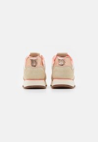 Beige und rosa Sportschuhe mit einem Veloursleder-Unterteil, einer gepolsterten Ferse und einem reflektierenden Akzent mit einem Logo auf der Rückseite.