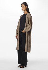 Pikk avatud ees cardigan heledast pruunist kudumifabricist, millel on soonikuga varrukad, koos sobiva musta topi ja tumedate teksadega.