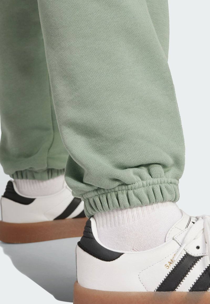 Light green elastic cuff sweatpants paired with white sneakers featuring black stripes and a textured gum sole.