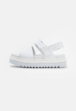 Hvid platformsandal med tyk rillede sål, åben tå, to justerbare spænderemme og slingback-design på en ensfarvet baggrund.